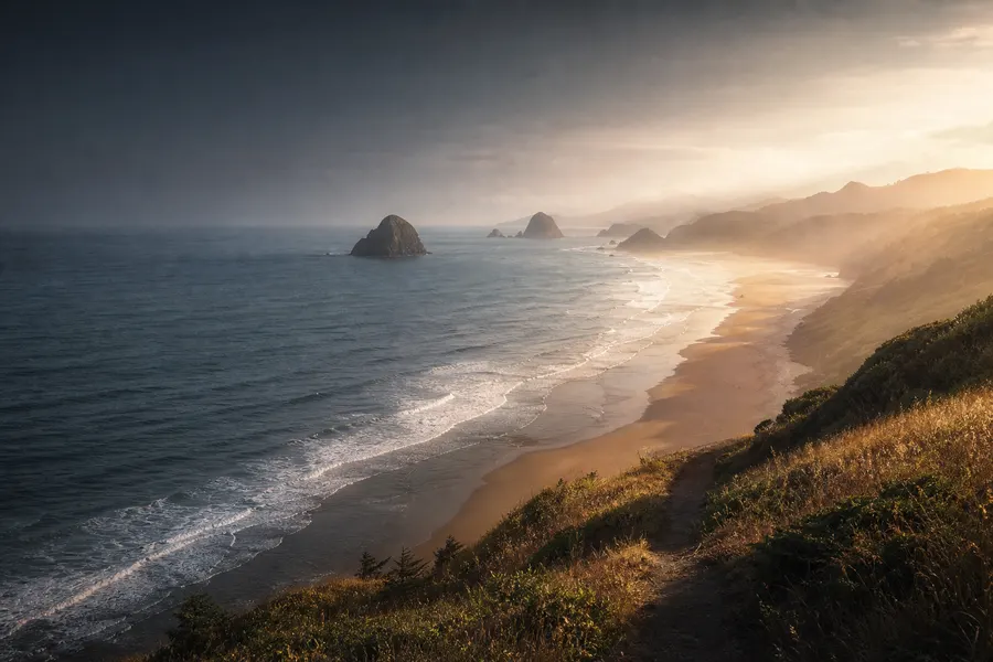 A broad Oregon beach and offshore sea stacks under late golden light